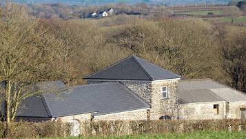 A stone building with a sloped roof, surrounded by trees and fields.