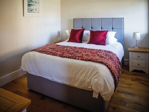 Een netjes opgemaakt bed met een grijs hoofdbord, een wit-rode deken en twee rode kussens.