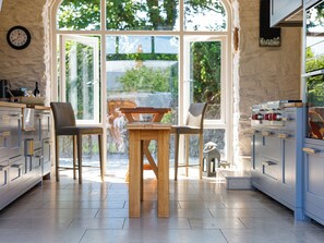 Een moderne keuken met een houten tafel, stoelen en uitzicht op de omgeving door grote ramen.