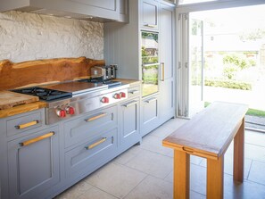 A kitchen with grey cabinetry, a wooden countertop, a gas stove, and a wooden table.
