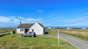 A single-story house with a sloped roof, a car parked in the driveway, and a clear blue sky.
