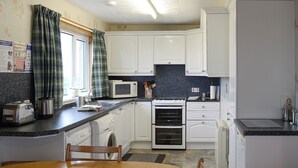 A compact kitchen with white cabinets, a microwave, an oven, and a sink. There's a dining table with chairs in the foreground.