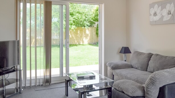 A living room with a sofa, a coffee table, a TV, and a sliding glass door leading to a backyard. - 1 bedroom accommodation in Broadstone, near Bournemouth (Broadstone, near Bournemouth)