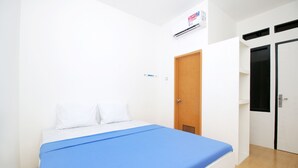 Une chambre à coucher avec un lit, des murs blancs, une porte en bois et une fenêtre.