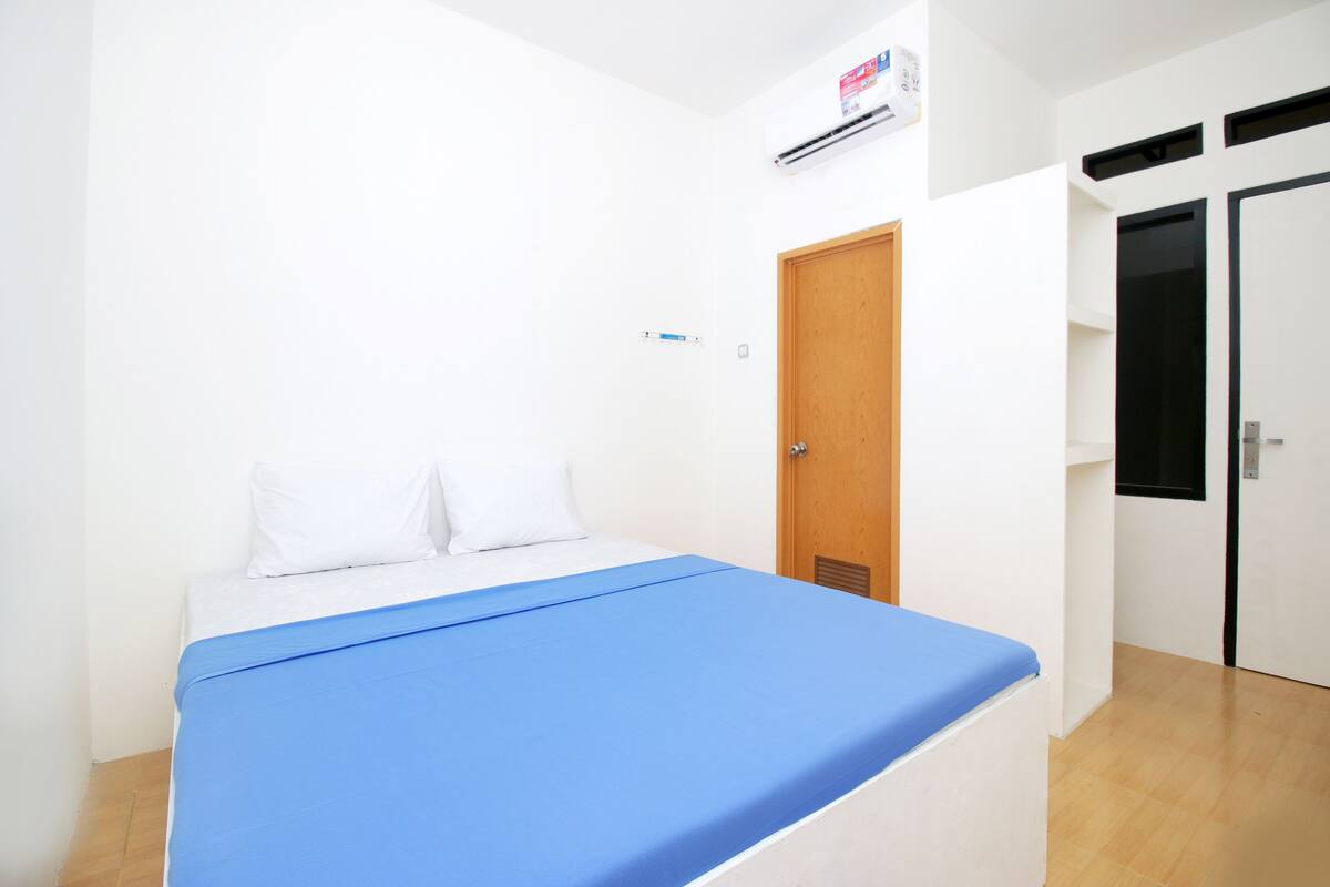 Une chambre à coucher avec un lit, des murs blancs, une porte en bois et une fenêtre.