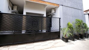 Un espace clos délimité par une clôture en métal, agrémenté de plantes en pot et comprenant un bâtiment à la façade grise et aux éléments décoratifs en bois.