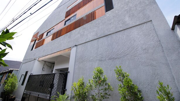 Un bâtiment moderne à la façade grise, doté d’un balcon avec des lattes en bois et d’un portail en métal noir.