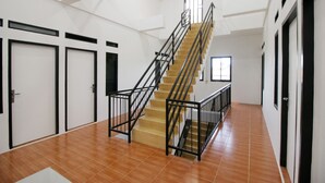 Un intérieur spacieux avec un escalier central, de nombreuses portes et un sol carrelé.