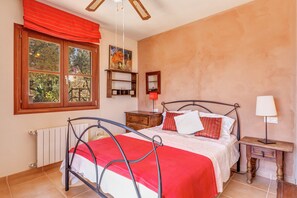 A bedroom with a bed, a nightstand, a window with curtains, a radiator, and a ceiling fan.