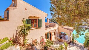 A Mediterranean-style villa with a terrace overlooking a clear blue sea, a small garden with cacti, and a balcony with outdoor furniture. - Fantastic Villa "Calima" with Sea Views, Loggia, Air Conditioning, and Wi-Fi (S'Estany den Más)