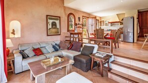 A spacious living area with a sofa, a coffee table, and a dining table with chairs. There is a kitchen in the background with a refrigerator and cabinets. - Fantastic Villa "Calima" with Sea Views, Loggia, Air Conditioning, and Wi-Fi (S'Estany den Más)