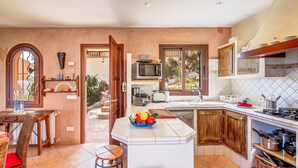 A kitchen with a central island, a dining area with a table and chairs, and a view through an open door. - Fantastic Villa "Calima" with Sea Views, Loggia, Air Conditioning, and Wi-Fi (S'Estany den Más)