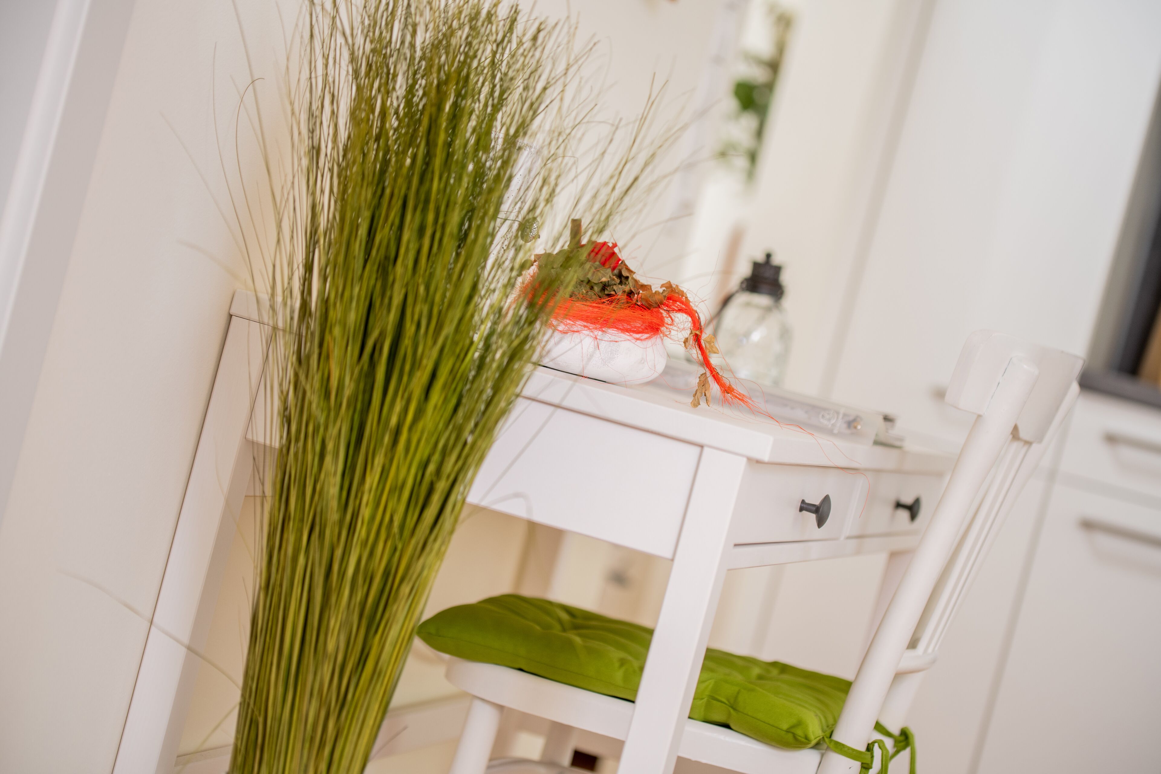 A white bedside table with a green cushion, a small plant, and a red object.
