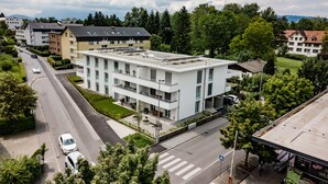 A modern multi-story building with balconies, a paved road, and surrounding greenery.