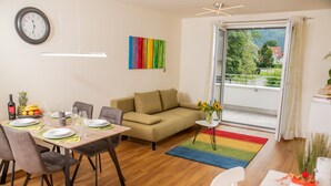 A modern living room with a dining area, a sofa, a coffee table, and a view of a balcony.