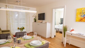 A modern dining area with a wooden table set for four, a television above, and a view into another room.