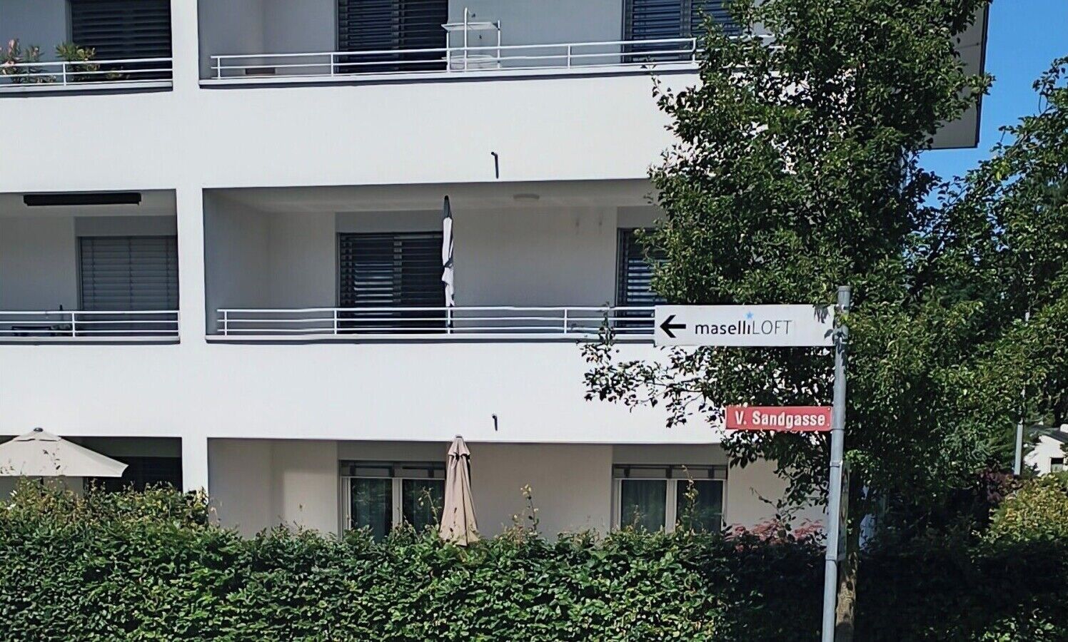 Ein mehrgeschossiges Gebäude mit Balkonen, einem Schild mit der Aufschrift 'maselliLOFT' und einem Straßenschild für 'V. Sandgasse'.