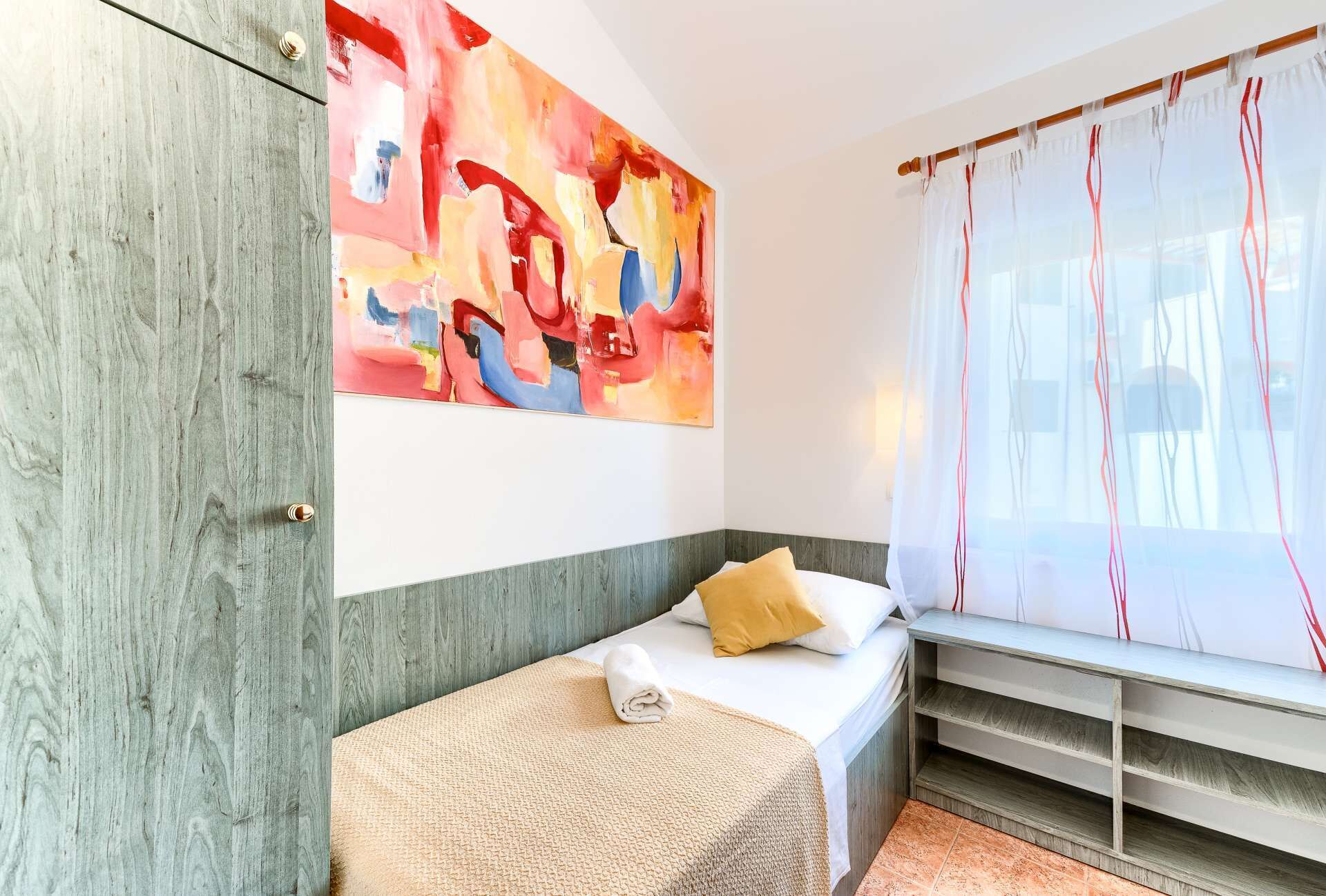 Une chambre à coucher avec un lit, un banc, un grand tableau abstrait et des rideaux en voile.