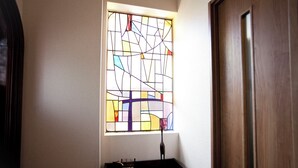 A stained glass window with geometric patterns, a black table with a vase and a book, and a wooden door. - Nagomi House (Tokyo)