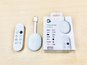 A Chromecast device, a USB cable, and a box with logos of various streaming services. - Nagomi House (Tokyo)