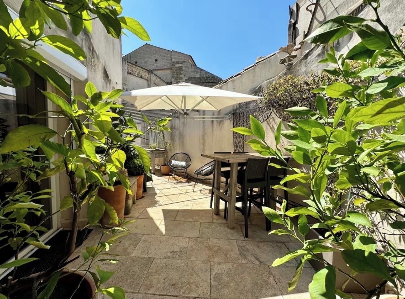 A courtyard with a table and chairs, surrounded by potted plants and a large umbrella.