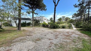 Une allée de gravier mène à une maison à l’extérieur blanc, avec un grand arbre en premier plan.