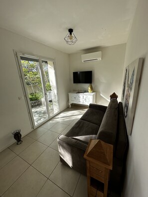 Un salón amplio con un sofá, un televisor montado en la pared y un ventanal corredero que da a un área exterior.