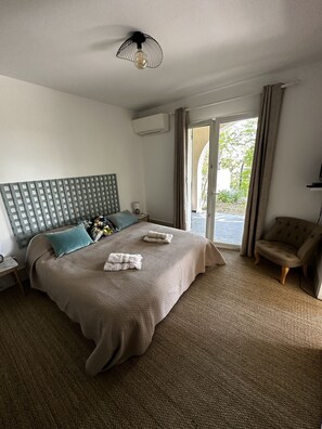 Una habitación de hotel con una cama grande, un cabecero, una silla, un escritorio, una lámpara y un equipo de aire acondicionado.