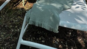 Deux fauteuils blancs, une couverture verte, une petite table avec une boisson et un verre contenant un liquide jaune.