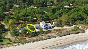 Una propiedad costera con una casa grande rodeada de abundante vegetación, una playa de arena y olas del océano.