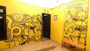 A hallway with yellow walls featuring cartoonish wall art and a wooden bench. - Kamar Keluarga Mangga Besar (Jakarta)