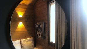 A circular window view of a cabin room with a bed, a painting of a wolf, and two wall-mounted lights. - Le Portail 13 - Outstanding apartment at the foot of the slopes (LES AVANCHERS VALMOREL)