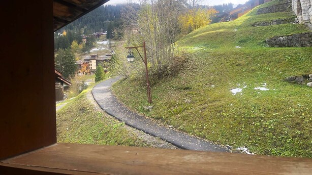 A view through a wooden structure, overlooking a winding path, grassy areas, and buildings in a hilly landscape. - Le Portail 13 - Outstanding apartment at the foot of the slopes (LES AVANCHERS VALMOREL)