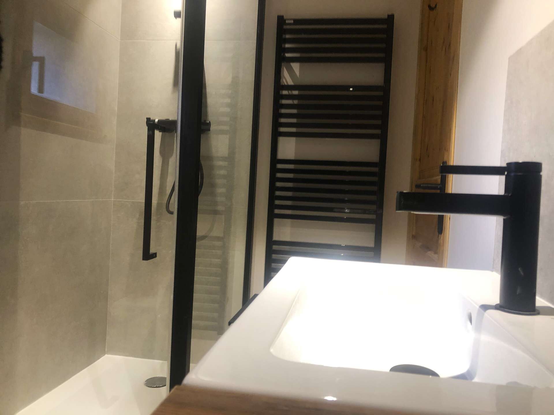 A modern bathroom with a glass shower enclosure, a white sink, and a black towel rack.