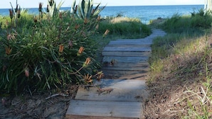 A wooden pathway leading to the beach, surrounded by greenery and overlooking the ocean. - L'Eden Corse (Biguglia)