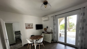 A modern living room with a wooden dining table, white chairs, a flat-screen TV, and a sliding glass door leading to an outdoor patio. - L'Eden Corse (Biguglia)