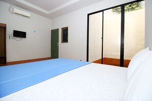 Habitación de hotel con cama, un tapete azul, televisor y puerta corrediza a un balcón.