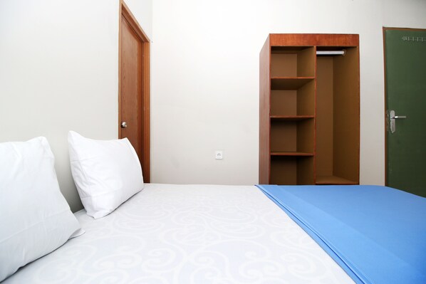 Un dormitorio con una cama, dos almohadas blancas, una colcha azul, un armario de madera y una puerta verde.