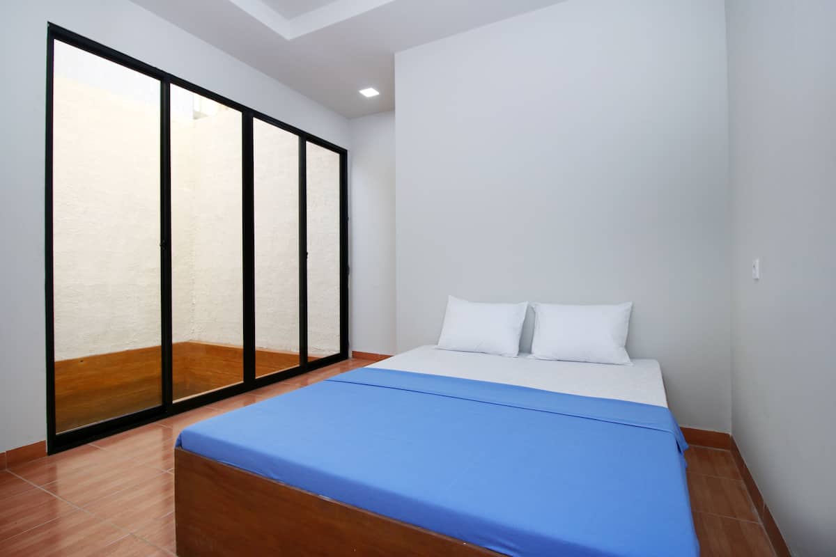 A bedroom with a bed, white pillows, a blue bedspread, and a sliding glass door leading to a balcony.