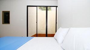 Une chambre à coucher avec un lit, une couvre-lit bleue, des oreillers blancs et une porte-fenêtre coulissante donnant sur un espace extérieur.