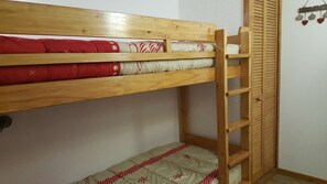 A bunk bed with a wooden ladder, a red and white patterned mattress, and a white mattress with red floral designs.