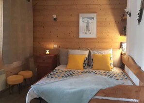 A wooden-paneled bedroom with a bed, two yellow pillows, a nightstand with a lamp, and a framed picture on the wall.
