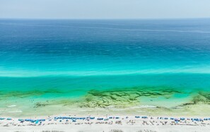 Ein Strand mit klarem türkisblauem Wasser, einem sandigen Ufer und blauen Sonnenschirmen.