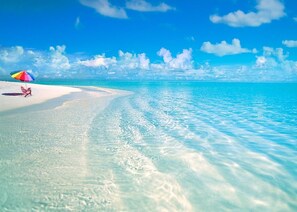 Una spiaggia con acque turchesi cristalline, una costa sabbiosa bianca e un ombrellone colorato.