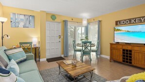 A living room with a sofa, coffee table, TV, and dining area with chairs and a table.