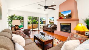 A spacious living room with a ceiling fan, a fireplace, and a large window offering a view of the outdoors. - UPSCALE Sedona VIEWS-heated POOL-golf-hot tub-Pball-tennis-fireplace-PRIVATE (Sedona)