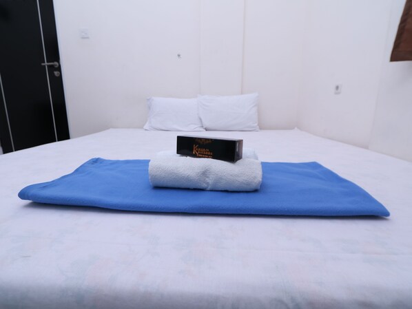 A neatly made bed with a blue blanket, white pillows, and a small black box on top.