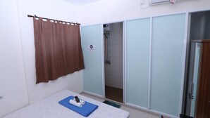 A bedroom with a bed, a blue mat, a brown curtain, and a sliding door leading to a shower area.