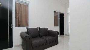 A modern living room with a black leather sofa, white walls, and a large window with brown curtains.
