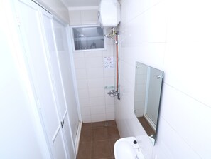 Un baño pequeño con azulejos blancos, un inodoro, cabina de ducha de vidrio y un espejo.